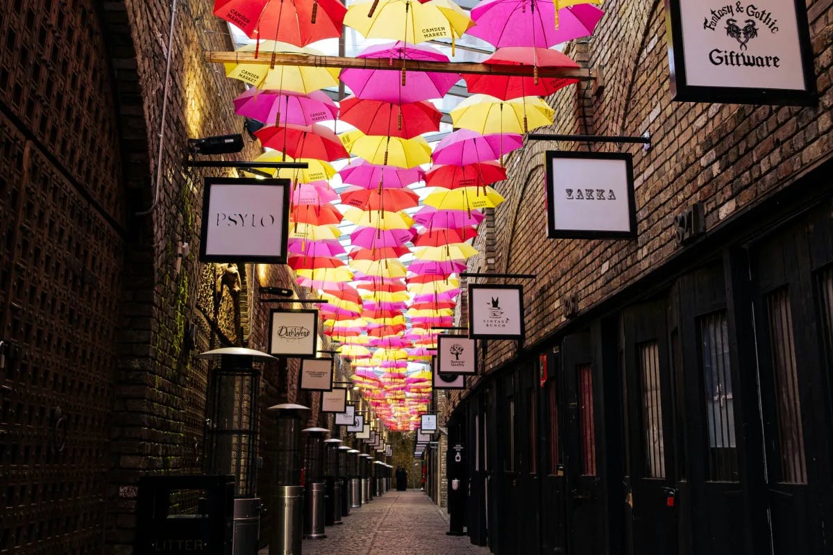 A narrow alleyway with pink, red and yellow umbrellas above 
