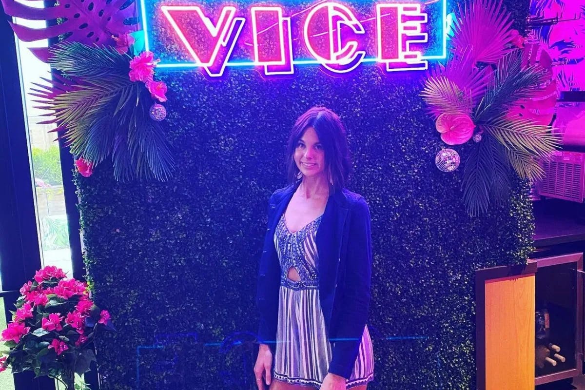 woman posing in front of a neon light and fake shrubbery