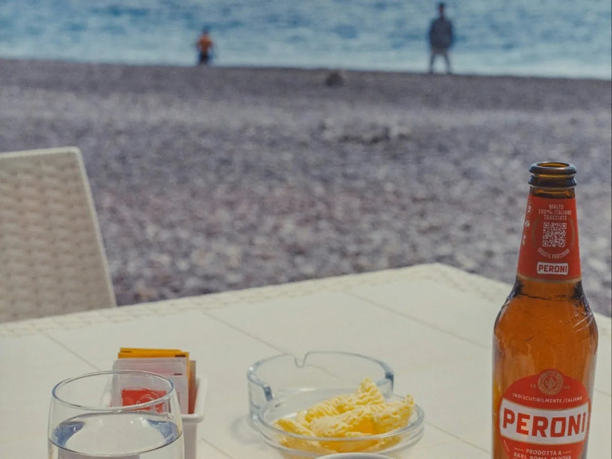 A table with beer and a bowl of chips on beach.