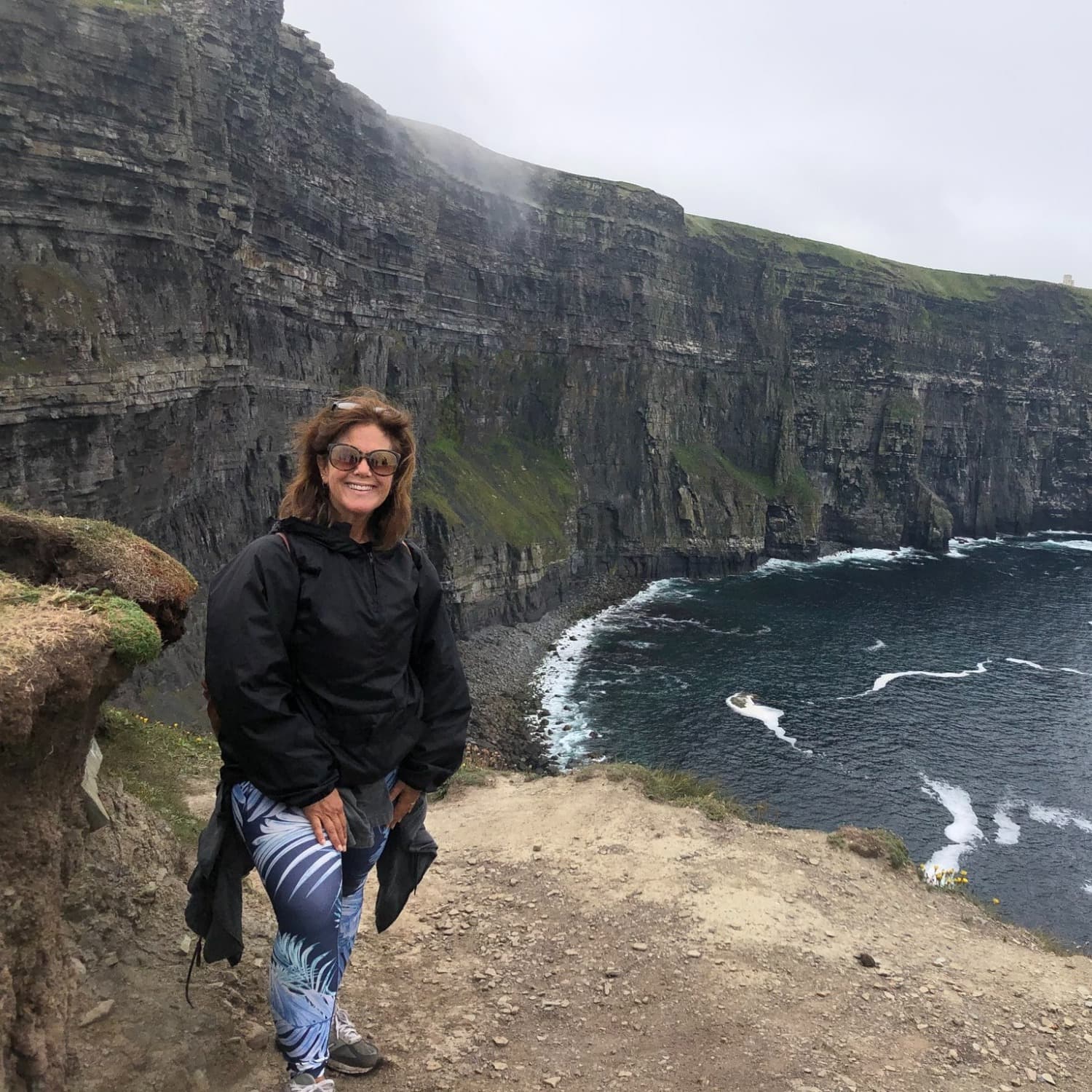 Travel advisor in front of a water body with cliffs on shore.