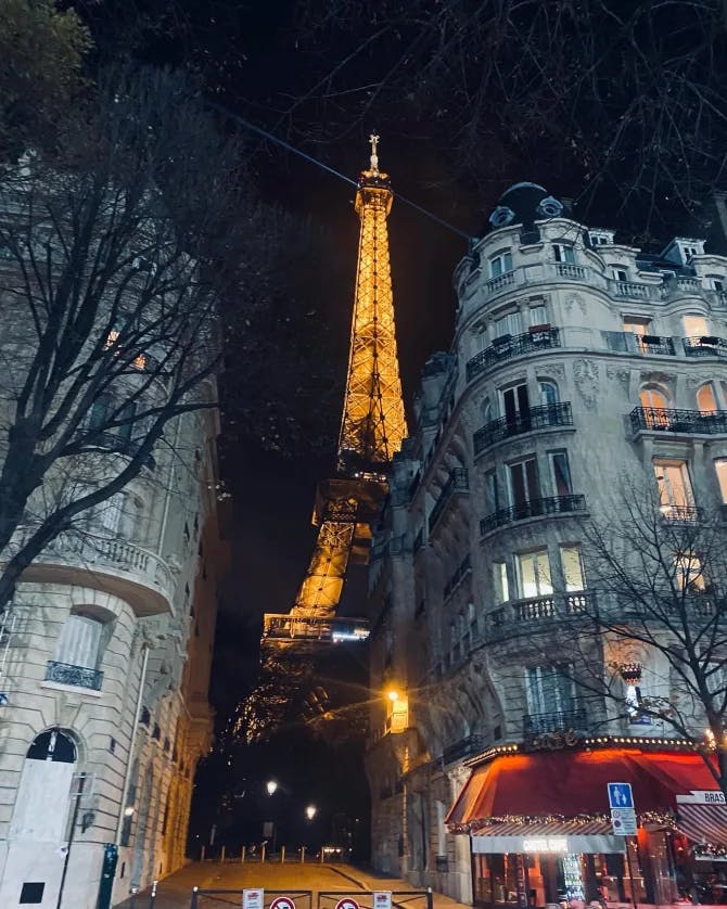 A nighttime view of the Eiffel Tower lit up behind french buildings