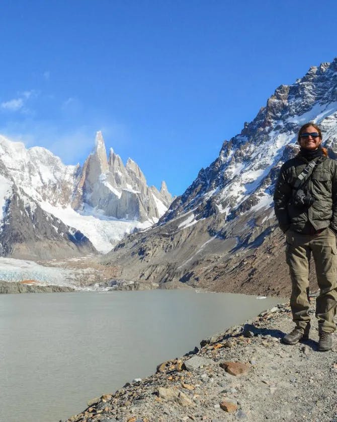 Ronny standing on a rocky path with a lake and snow covered mountains to his left
