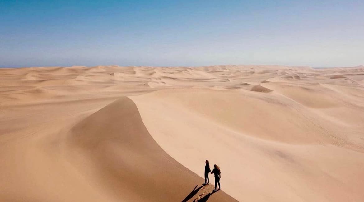 A picture of a large sand dune with people walking along it.