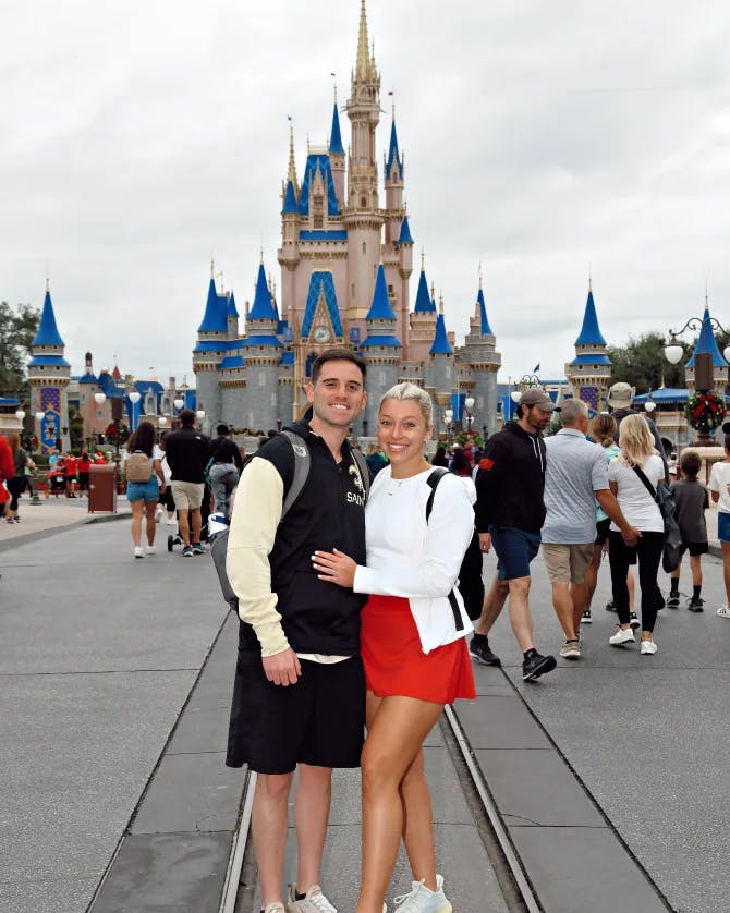 Zoe and partner posing in front of the castle at Walt Disney Land surrounded by traveling tourists