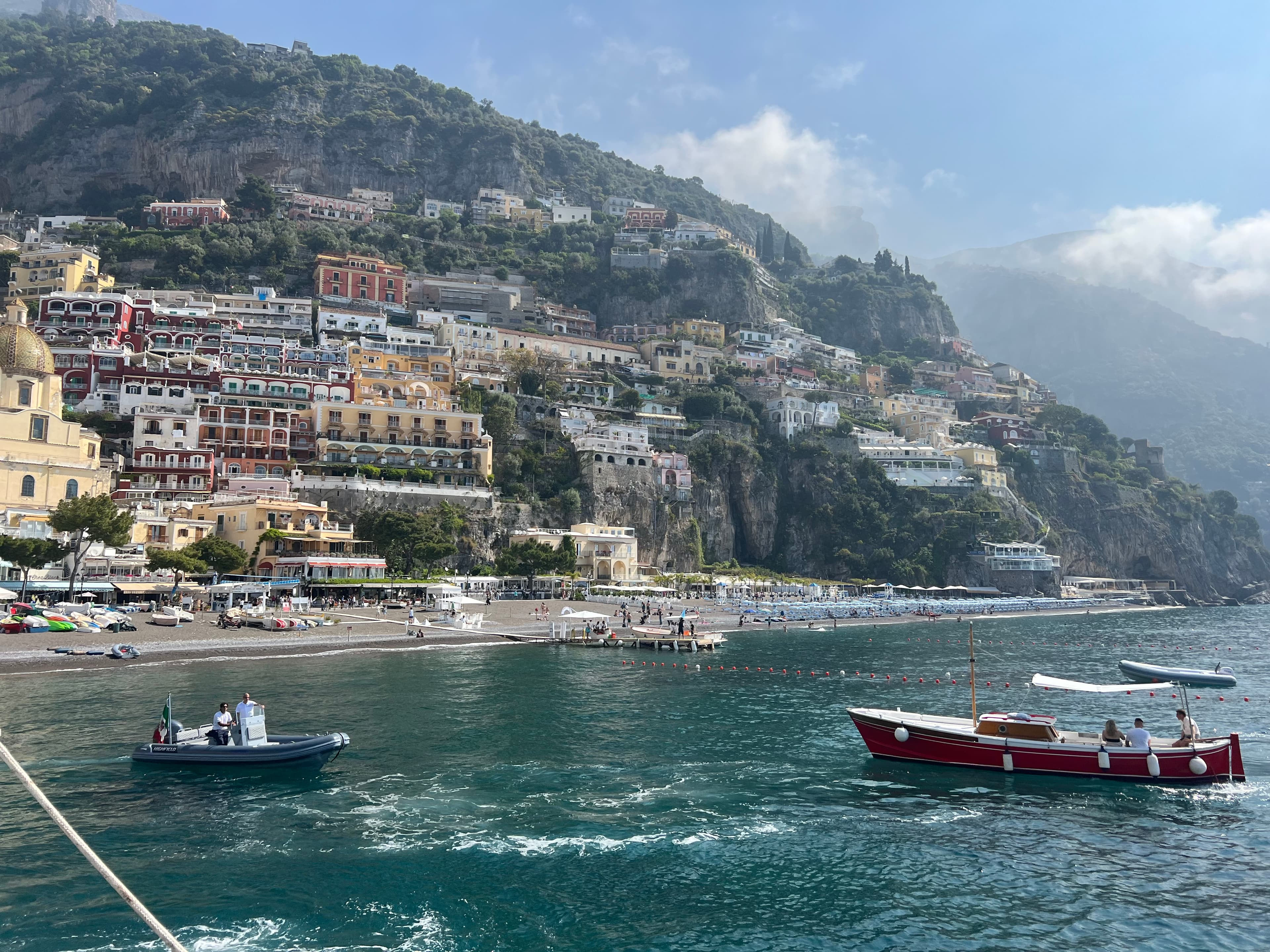 Boats sailing in the sea in front of a European coast filled with colorful buildings