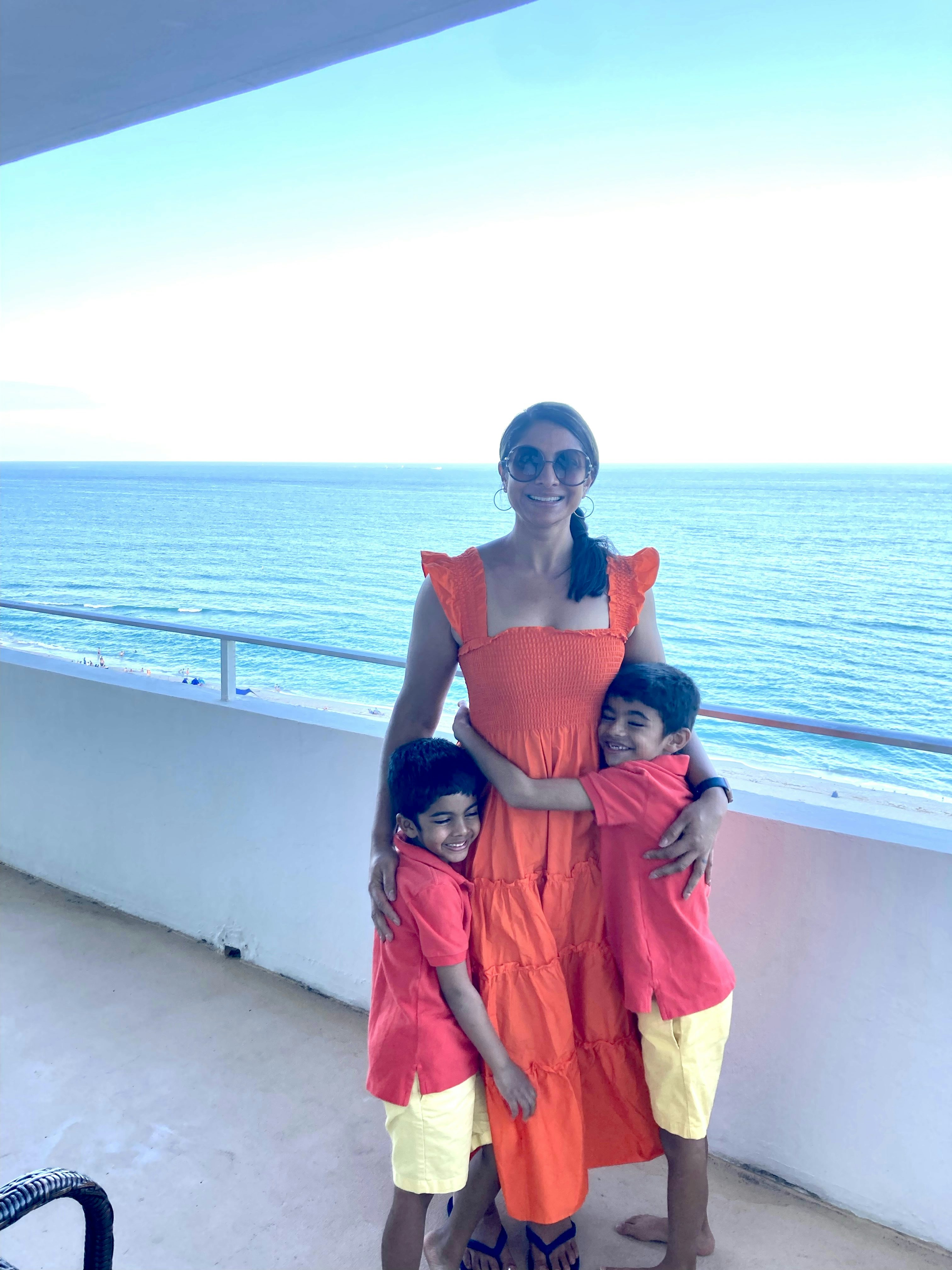 Travel Advisor Pallavi Patil in a red dress with her two kids and water in the distance.