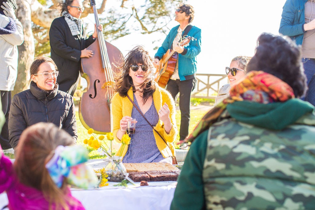 Travel Advisor Karen Cook in a purple dress and yellow sweater with musicians playing in the background.