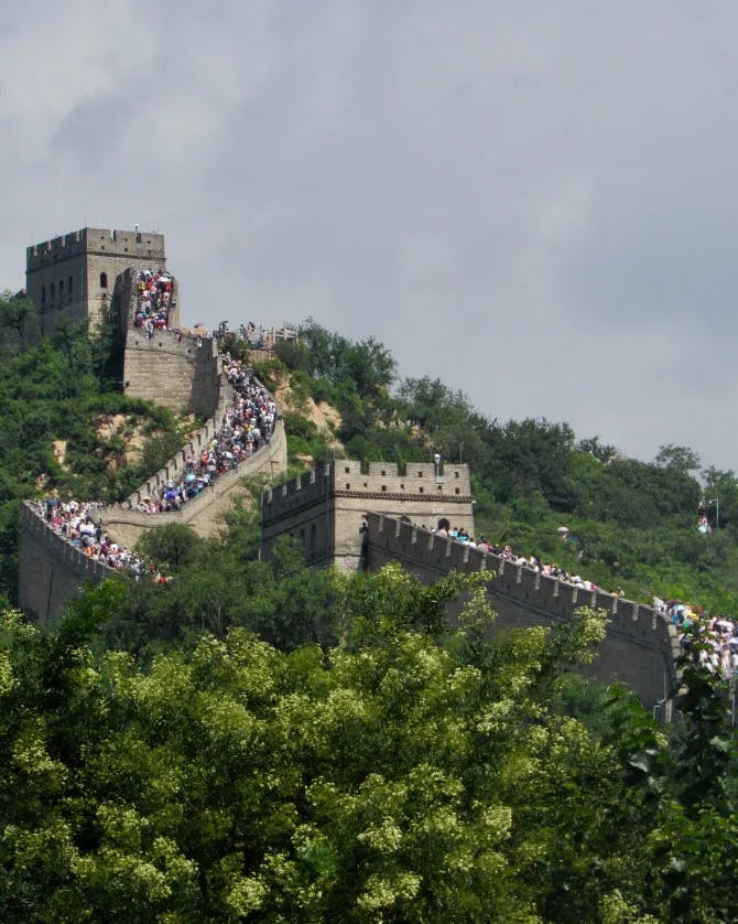 A picture of the Great Wall of China surrounded by trees and tourists on a cloudy day