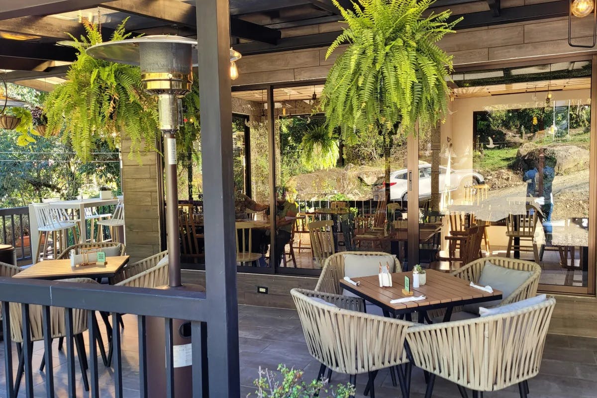 A picture of an outdoor restaurant with white chairs, brown tables and hanging plants.