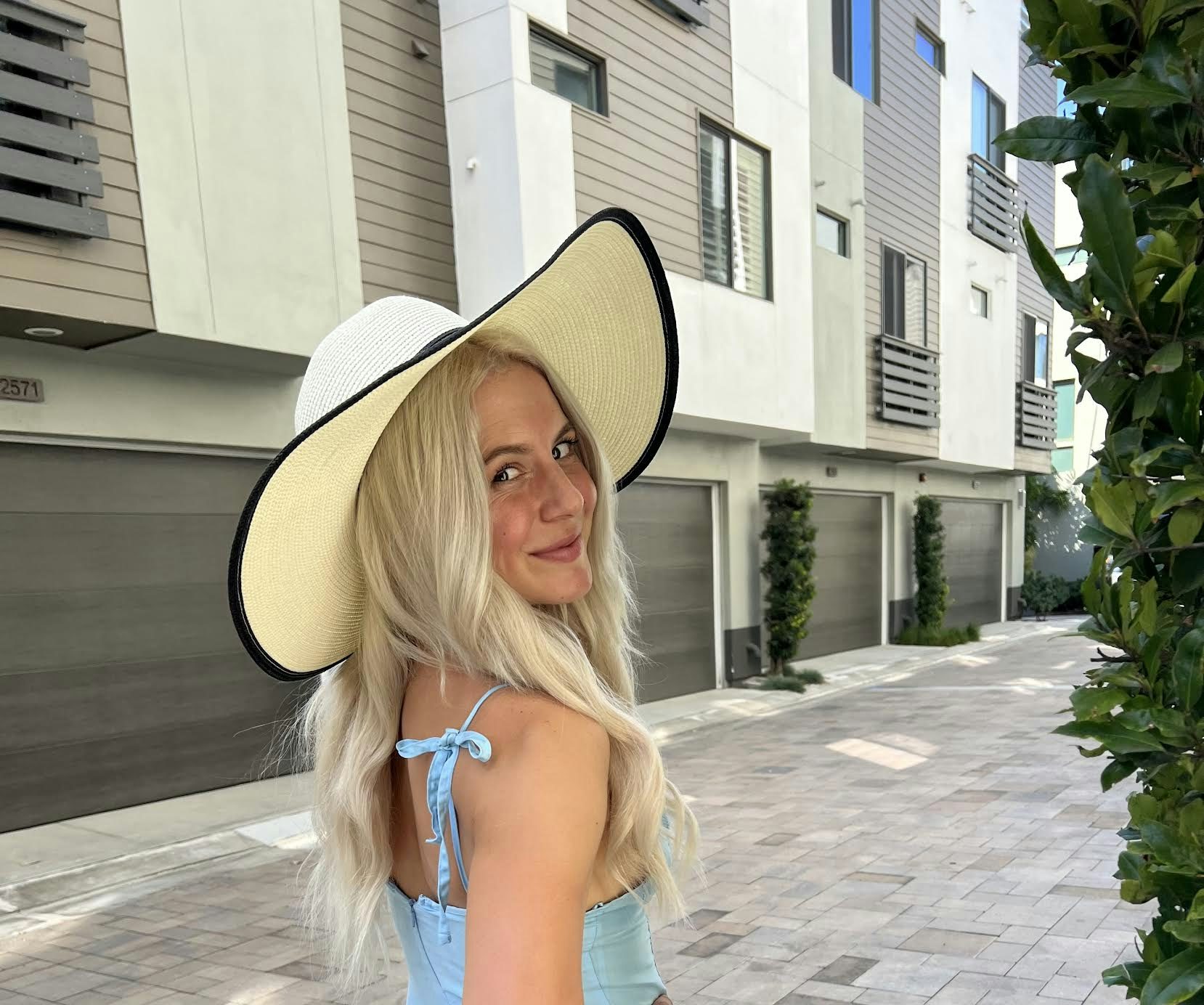Travel advisor Maddy Mazzeo wears a blue dress and large brim sun hat on a quiet city street