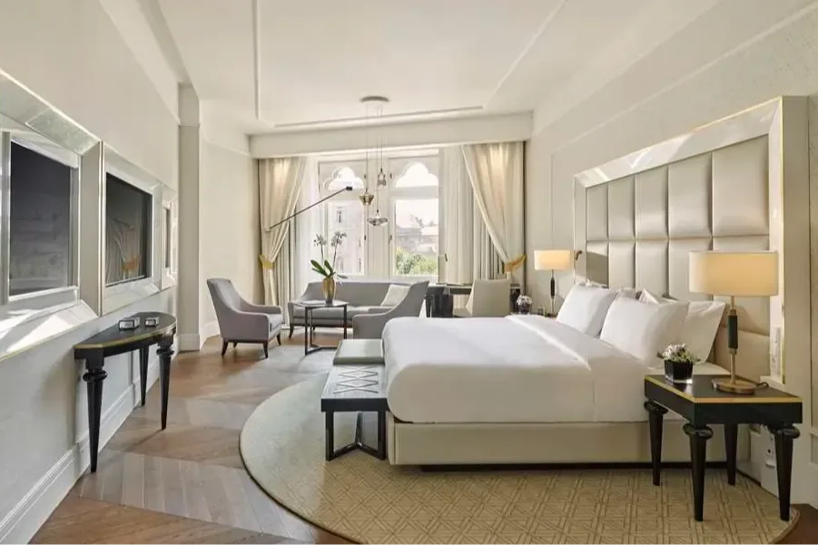 a light-filled hotel room with wooden flors and elegant windows flanked by white drapes