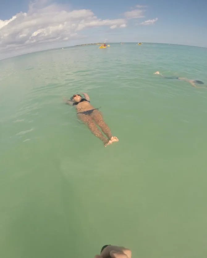 A fisheye lens view of Amber floating on green water in a black swimsuit.