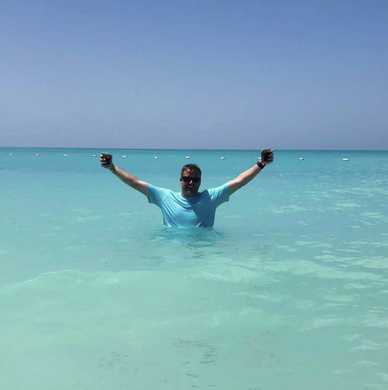 Travel advisor Michael in a blue shirt standing in water with his arms outstretched above him. 