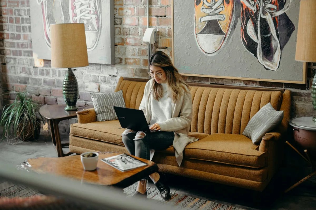 In a trendy, contemporary apartment, a woman sits on a couch while working on her laptop