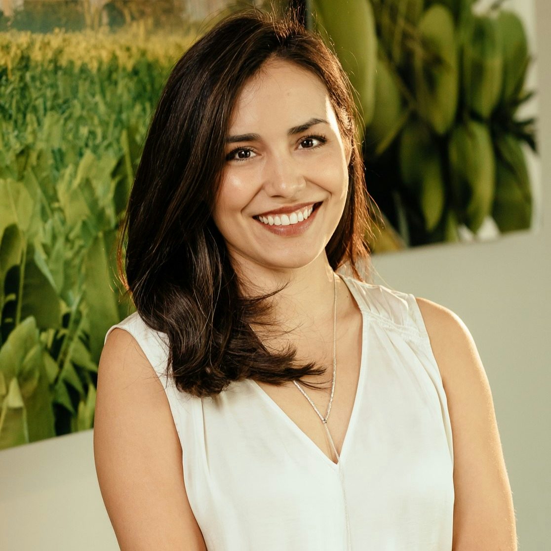 Travel Advisor Daniella Velazquez de Leon wears a white tank top and smiles in front of a green plant