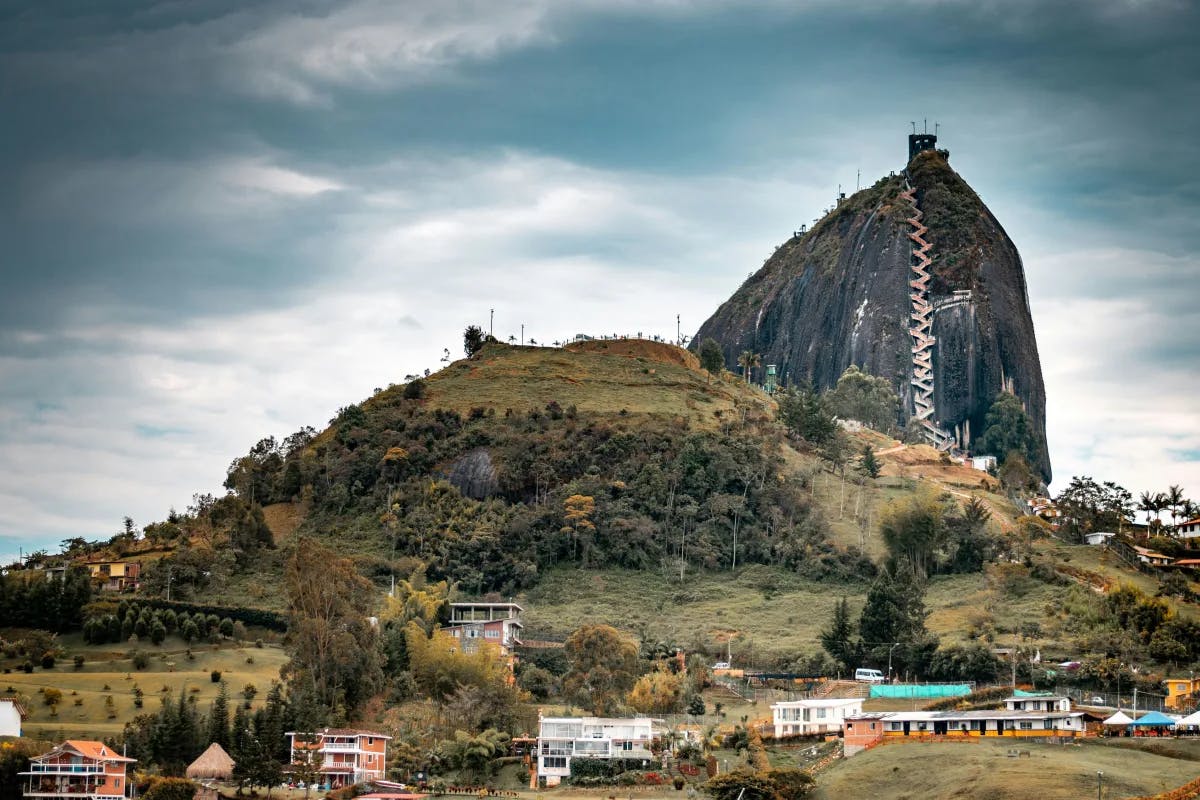 Guatape - a large rock on top of green-brown mountains on a cloudy day.