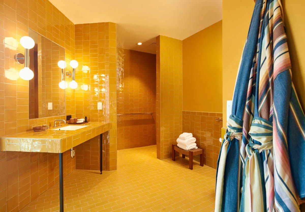 colorful robes hanging in a yellow tiled bathroom