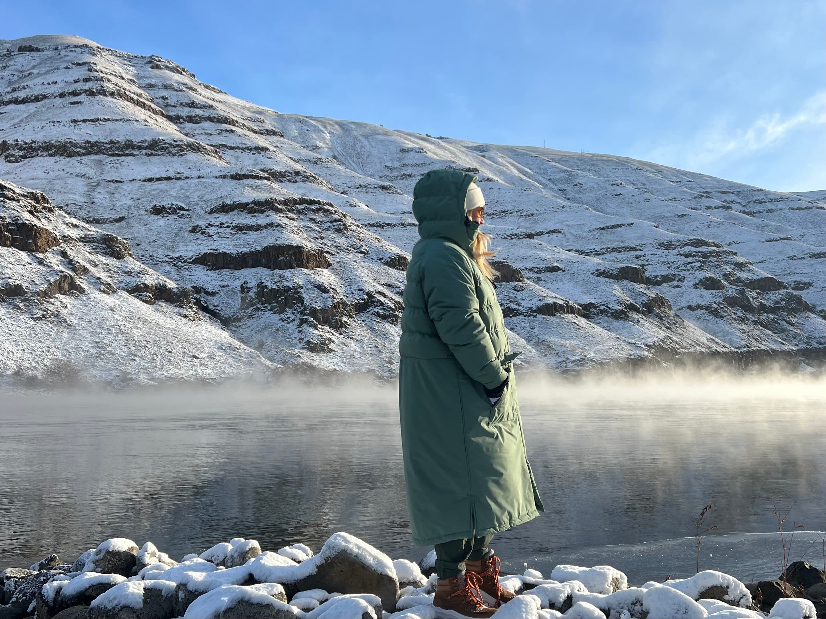 snow covered mountains and a frozen lake with steam coming off of the shore line.