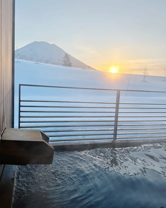 A water feature near a metal fence looking out to a snowy mountain and sunrise 