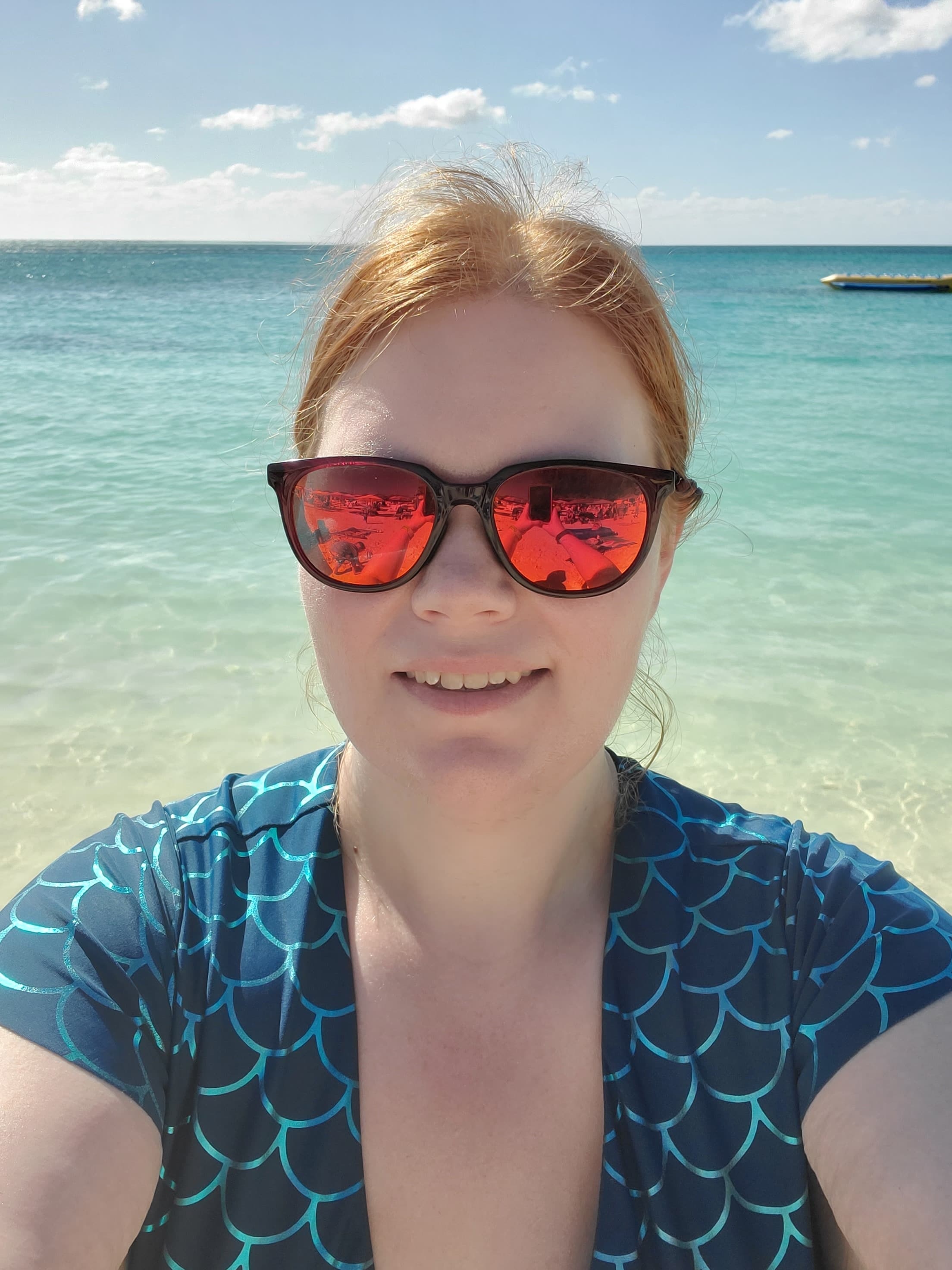 Picture of Jeanne at beach wearing a blue patterned top and orange tinted sunglasses