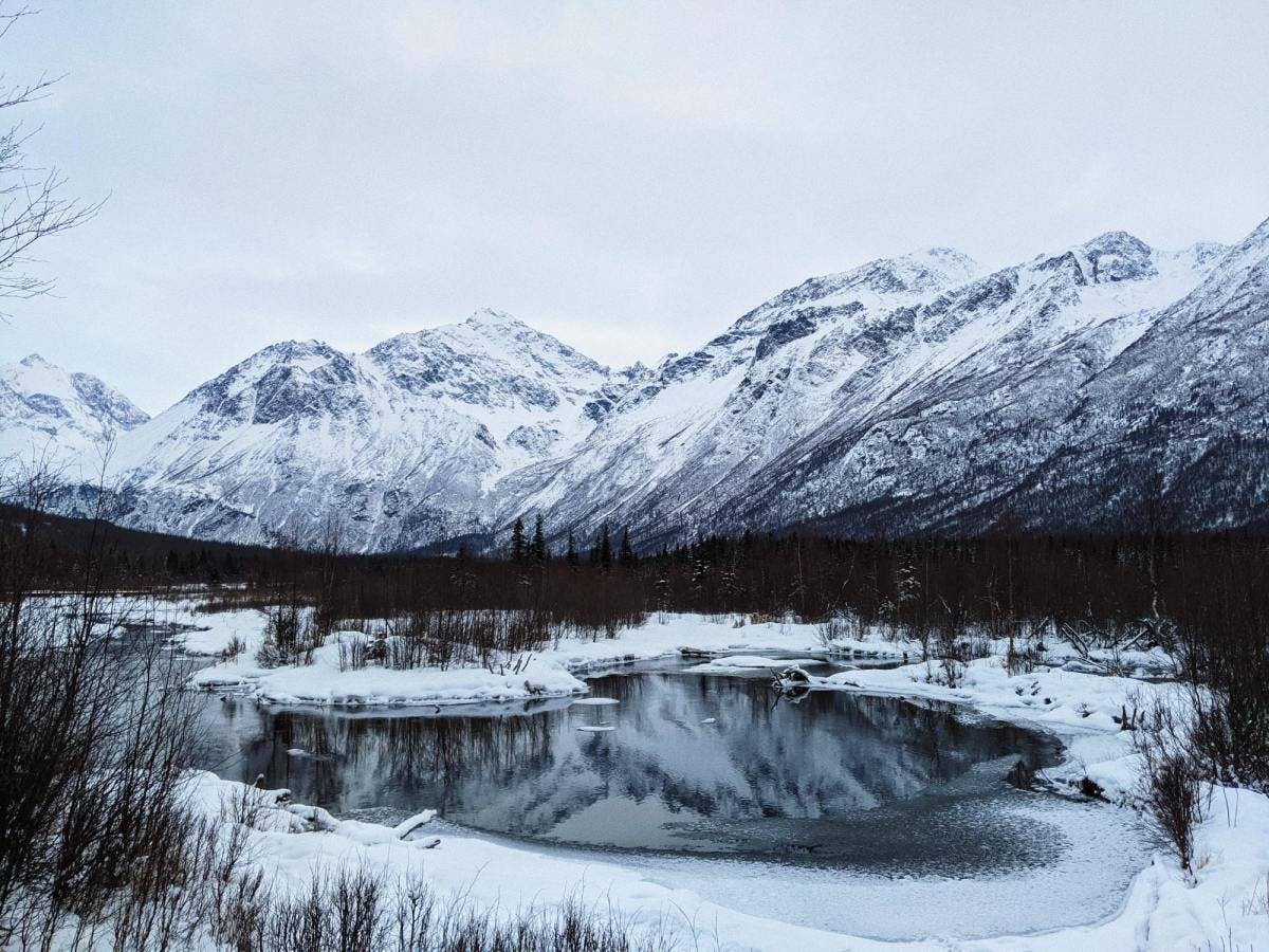 Snowy mountains behind icy lake during a chilly winter day in Anchorage, Alaska. 