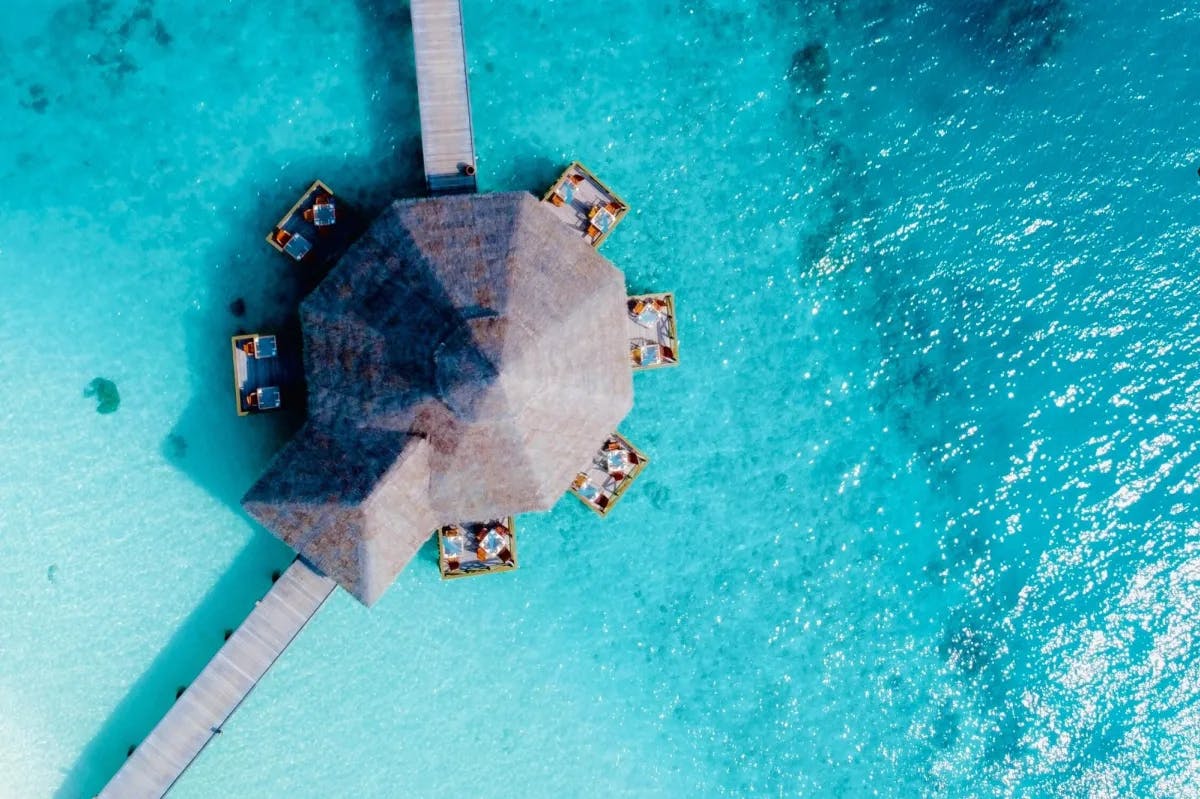 Aerial view of an overwater-bungalow-style restaurant surrounded by crystal-blue waters in the Maldives