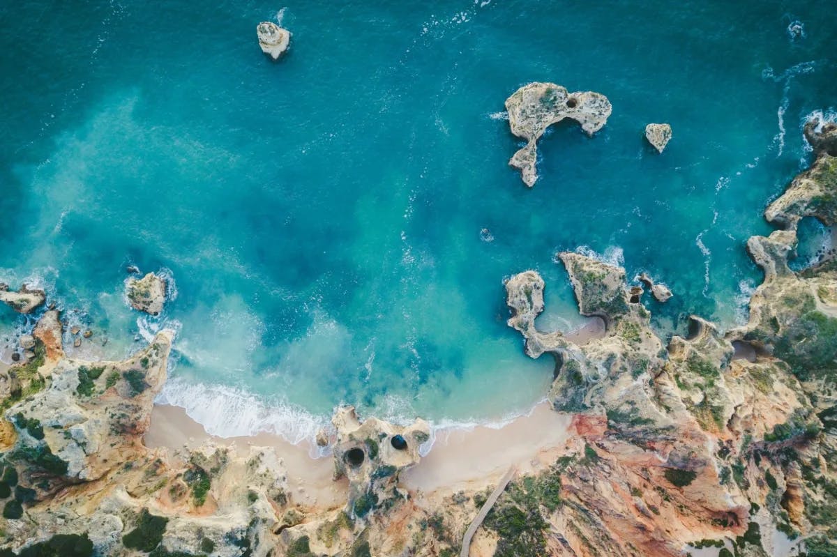 Saphire- and turquoise-blue water clashes with rough yet vibrant rock formations and soft white sand in Lagos, Portugal