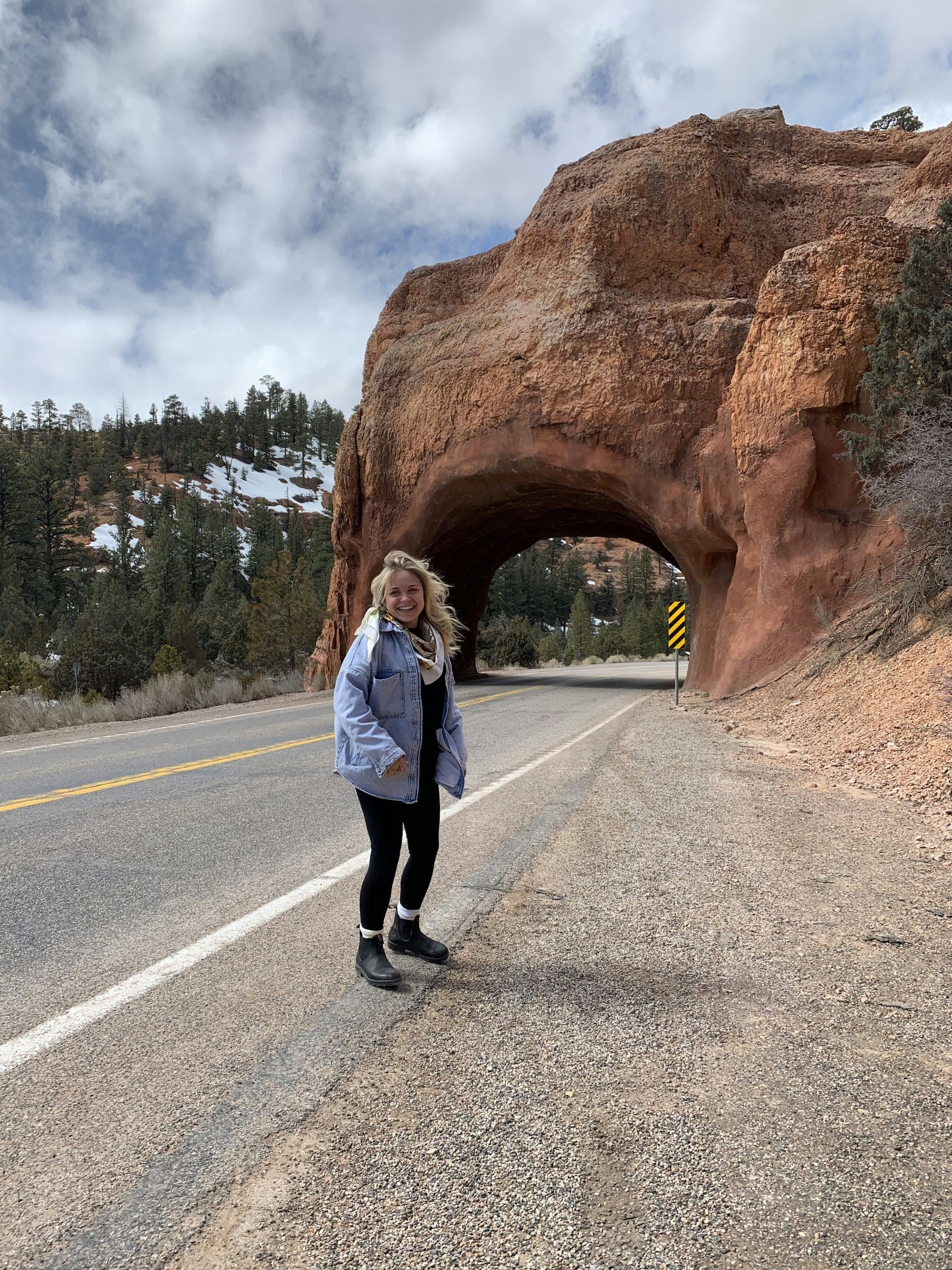 Travel Advisor Jessica Fappiano stands on a road in front of a natural stone arch wearing a jean jacket and hiking boots