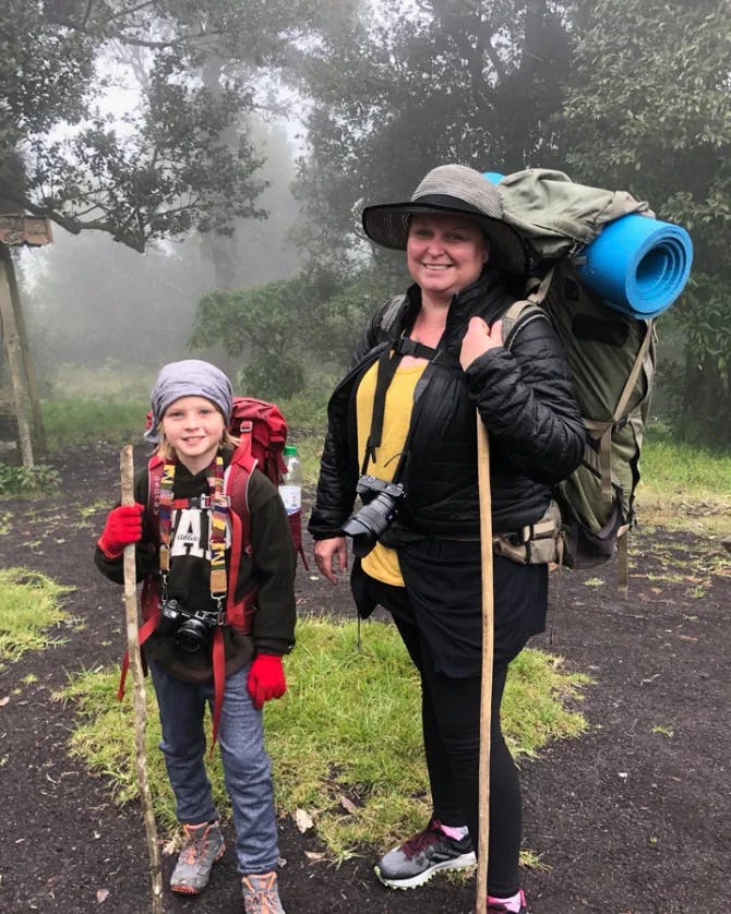 Karilyn with her young son, both suited up with hiking and camping gear, amidst the great outdoors on a foggy day.