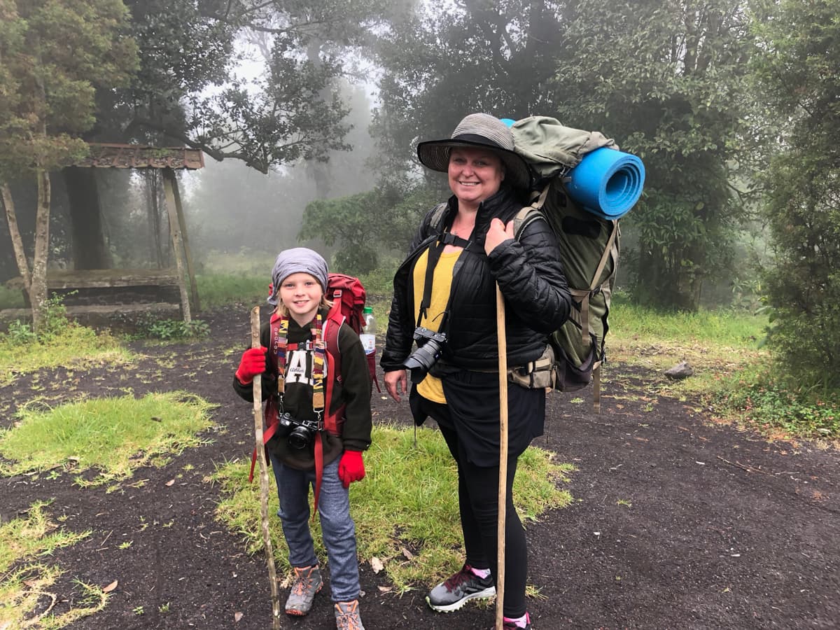 Karilyn with her young son, both suited up with hiking and camping gear, amidst the great outdoors on a foggy day.