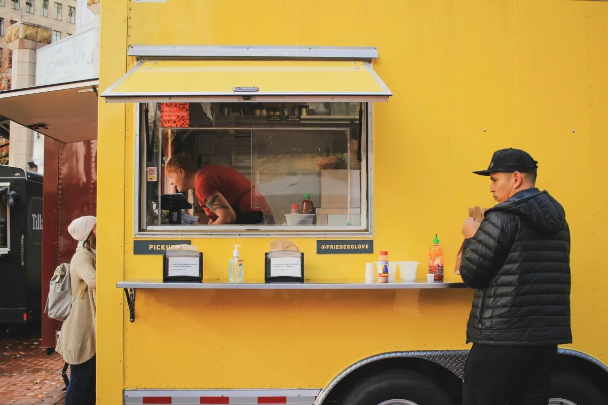 a man sips a drink outside of a yellow food truck