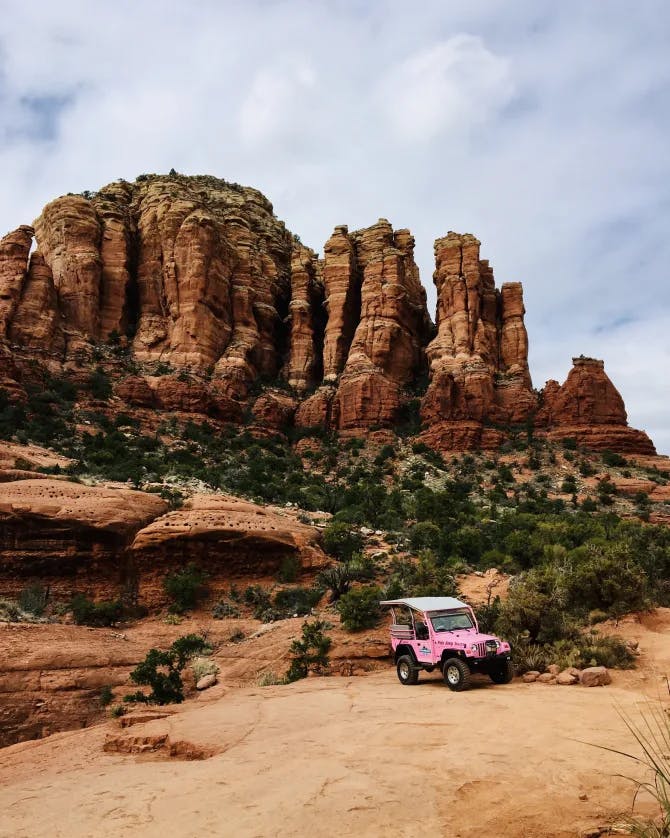 A pink jeep in Sedona surrounded by red rocks, trees and dirt roads.