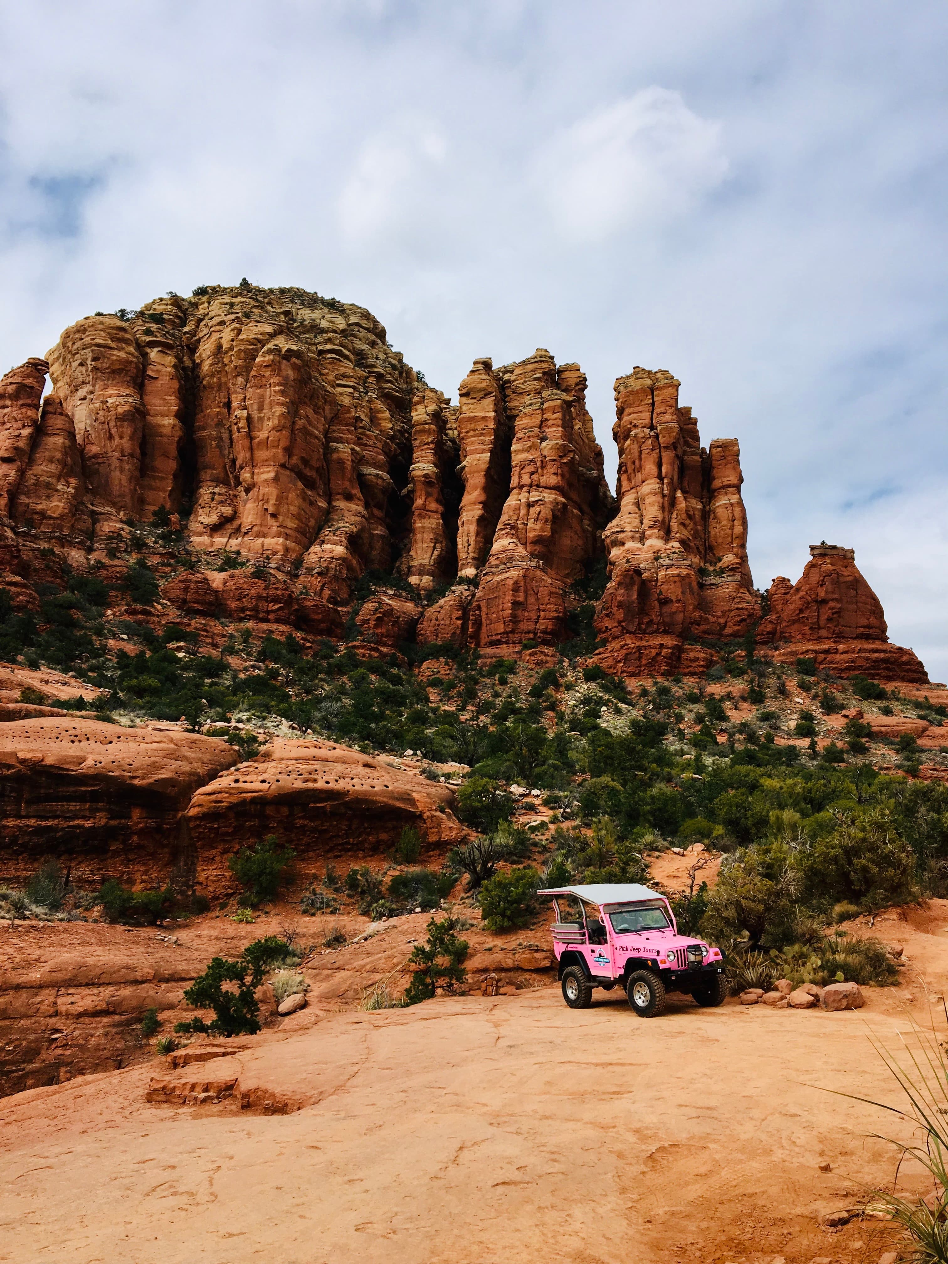 A pink jeep in Sedona surrounded by red rocks, trees and dirt roads.