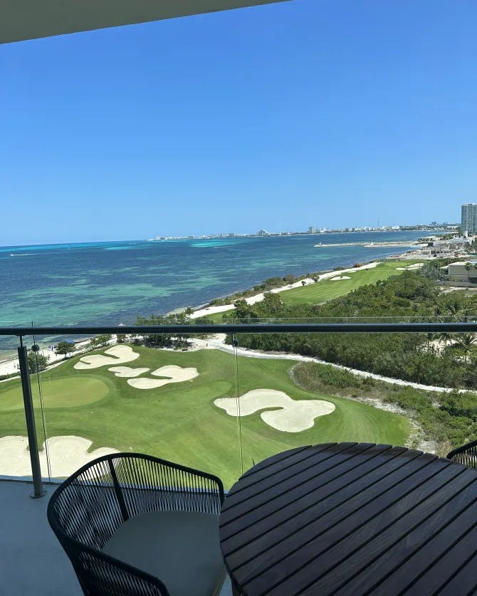 A picture of the grassy green view Dreams Vista Cancun Golf & Spa Resort and sea from a balcony with a table 