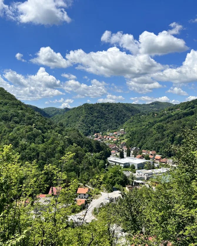 Photo of a green mountain range with a town in the middle set beneath the blue sky and white clouds