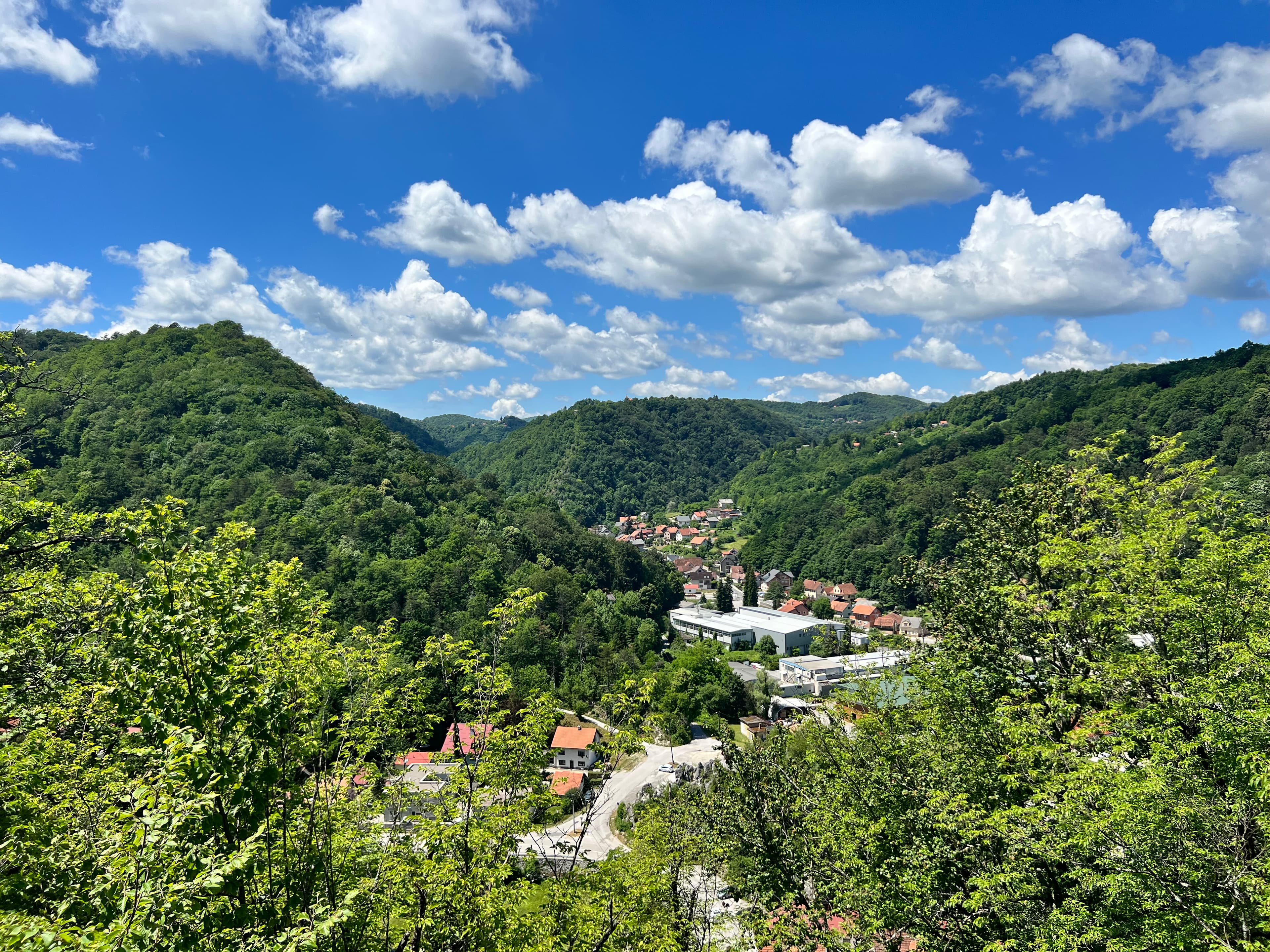 Photo of a green mountain range with a town in the middle set beneath the blue sky and white clouds