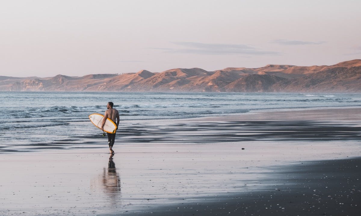 Surfer walking towards the sea with surfboard in North Island, NZ. 