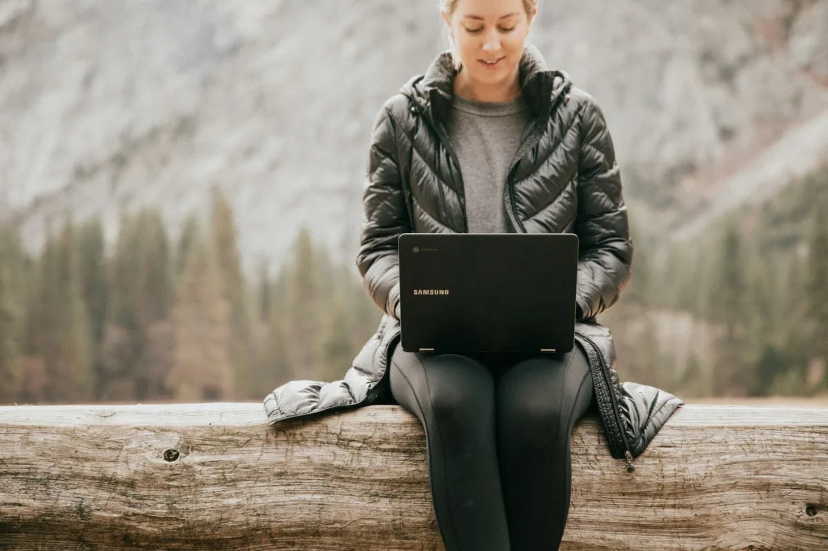 A woman works remotely from her satellite-connected computer in the middle of a forest