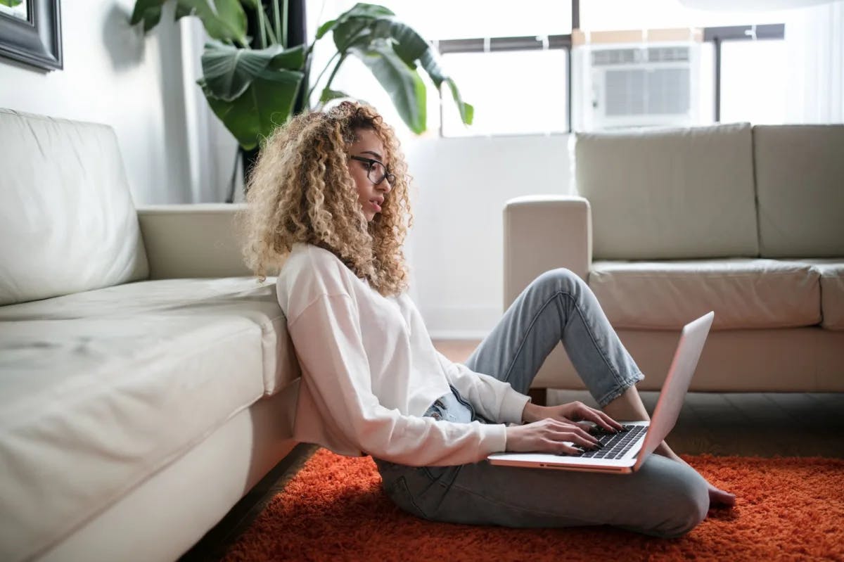 In a stylish apartment, a women lounges on shag carpet while working on her computer