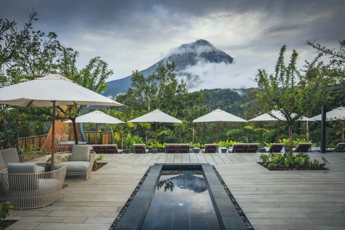 A sleek wooden pool deck at Nayara Tented Camp Costa Rica with a view of a volcano