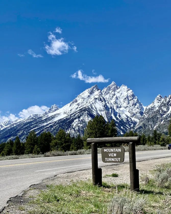 A national park sign in front of snowy mountains and a dirt road