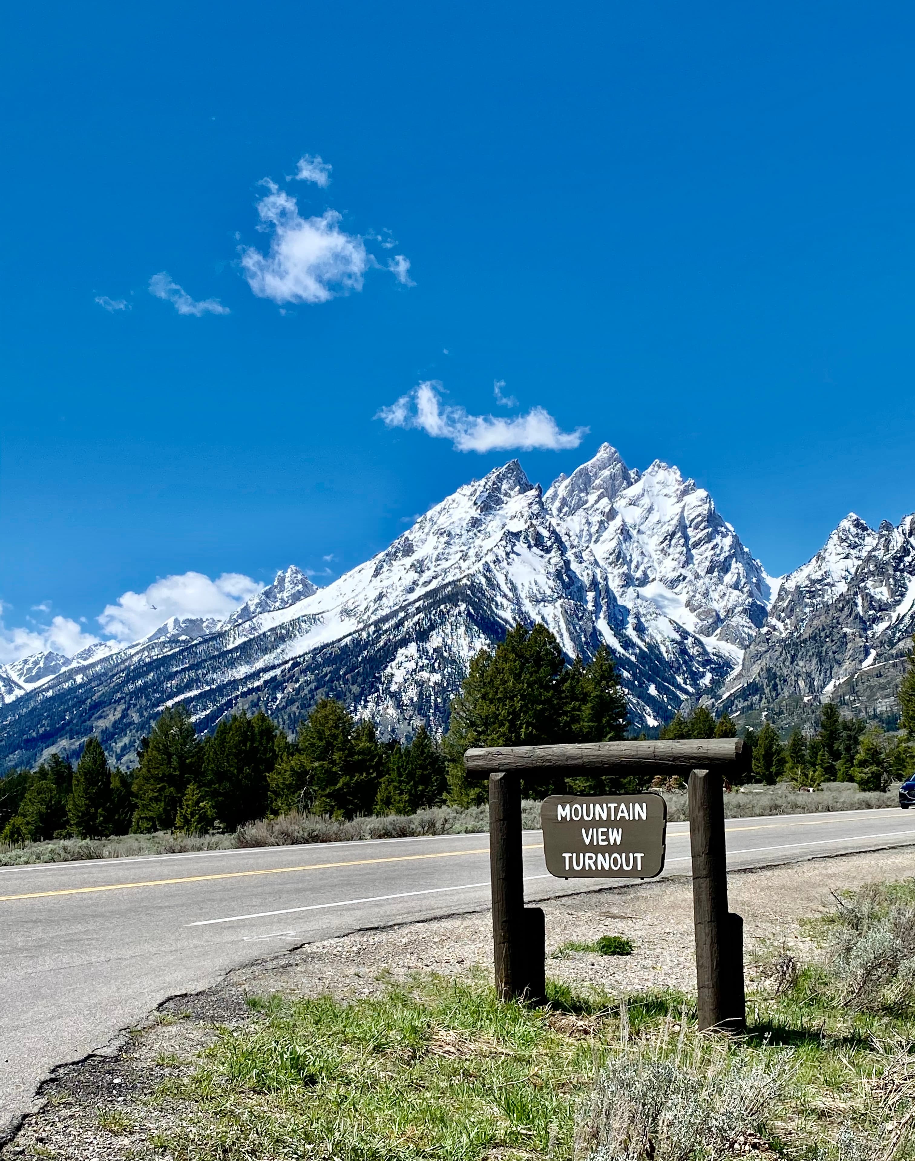A national park sign in front of snowy mountains and a dirt road