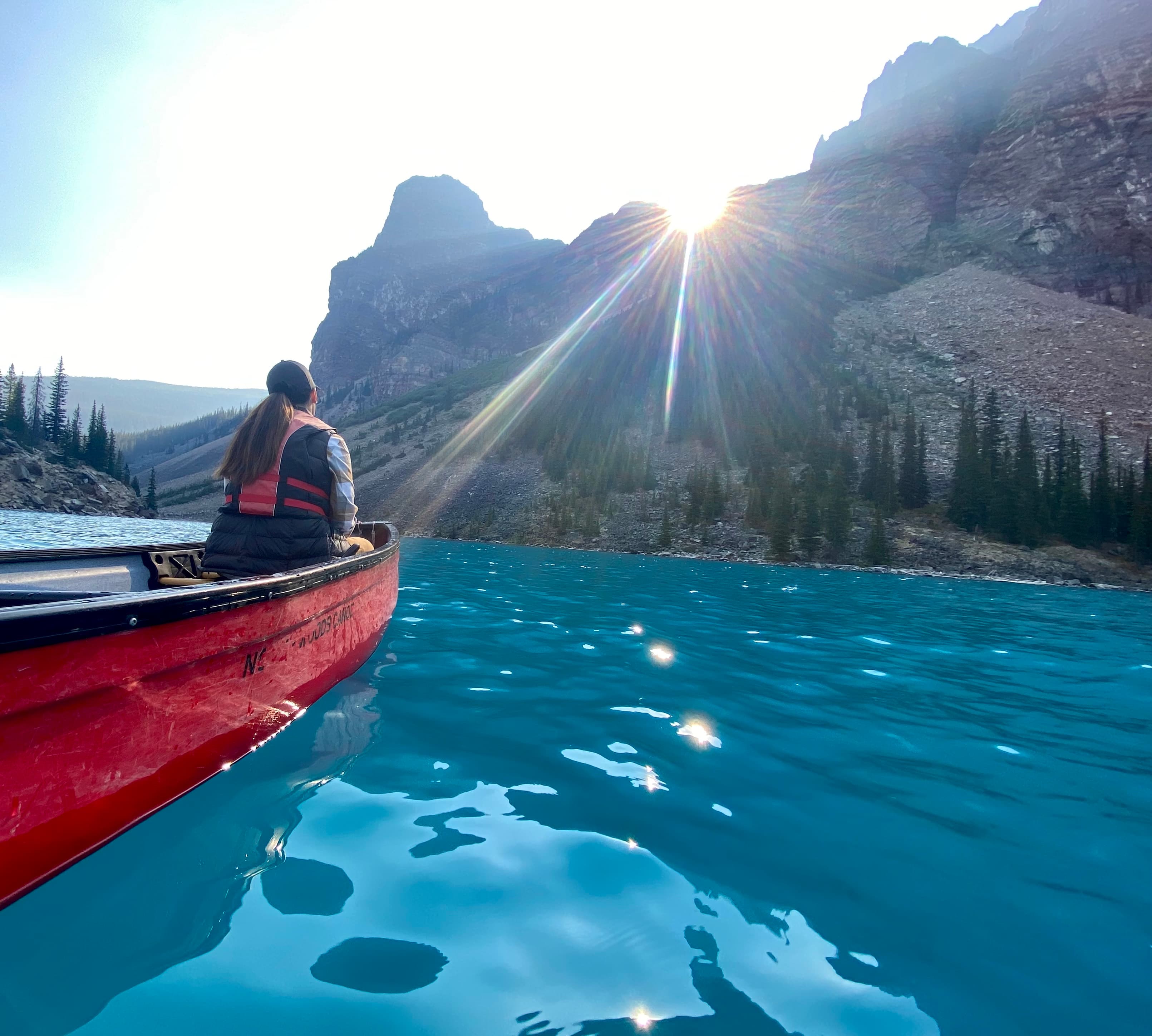 A woman sitting in a canoe on a clear blue lake with the sun shining.