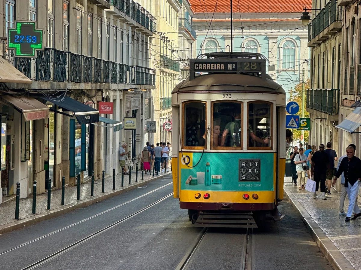  A yellow and teal tram between city buildings during daytime.