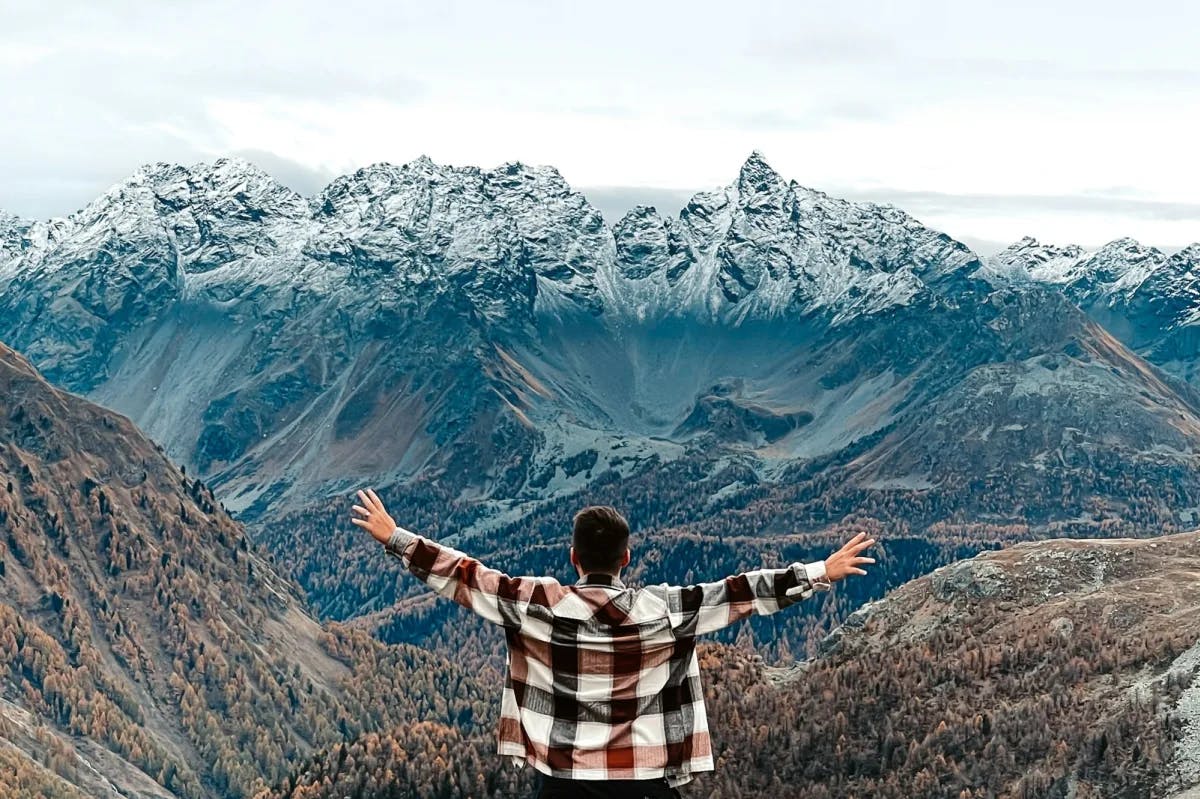 A man stands before the Swiss Alps, arms spread out gesturing at the majesty of the view and representing the wide options travel agents can choose for marketing