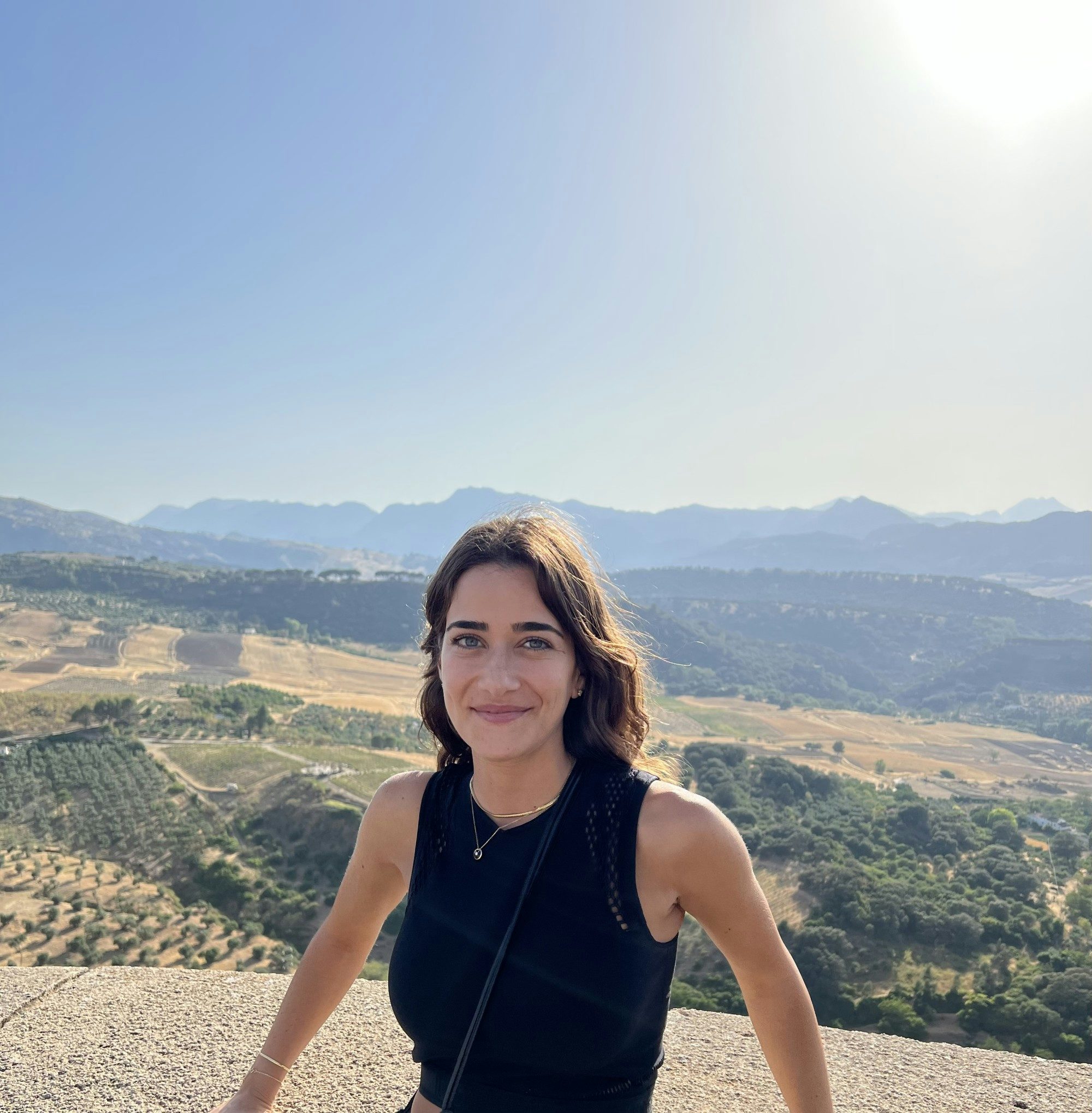 Travel advisor Deemah Bader in a black tank top smiling in front of a sunlit valley
