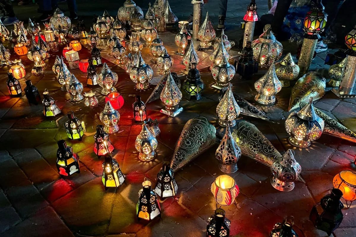 Dozens of ornate, metal Moroccan candle lanterns are lit on the ground in Jemaa el-Fnaa Square in the Marrakech Medina