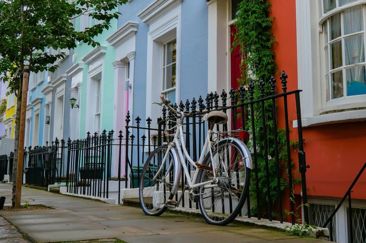 a white bicycle leans against an iron fence in front of pastel-hued houses