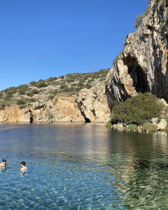 Two people swimming in a lake near a large rock formation