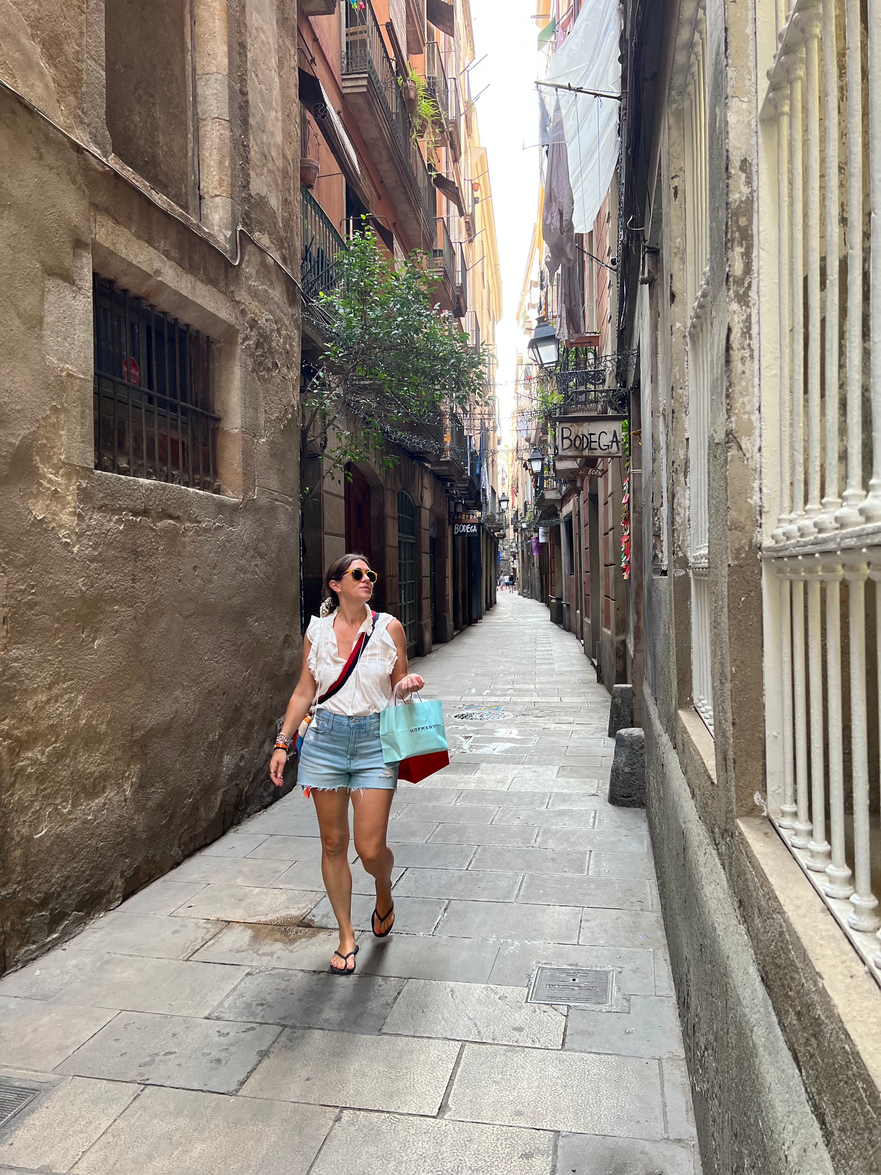 Latha walking down a narrow street surrounded by stone buildings and plants in Europe.